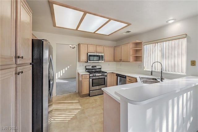 kitchen with light brown cabinetry, stainless steel appliances, sink, and kitchen peninsula