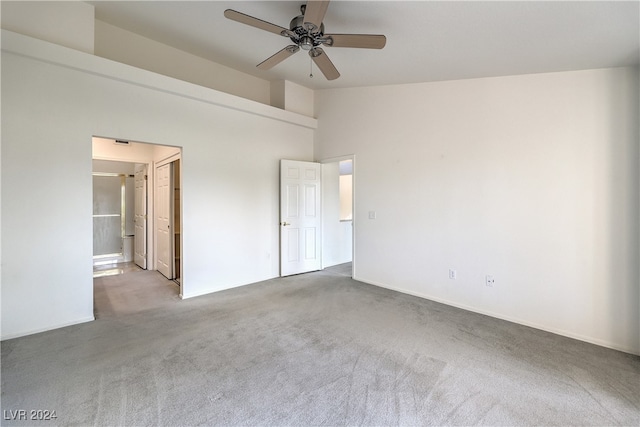 unfurnished bedroom featuring a high ceiling, connected bathroom, light carpet, and ceiling fan