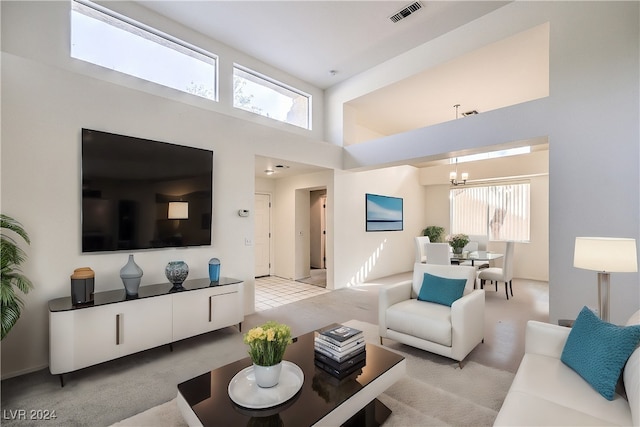 living room with a towering ceiling, a chandelier, a wealth of natural light, and light colored carpet