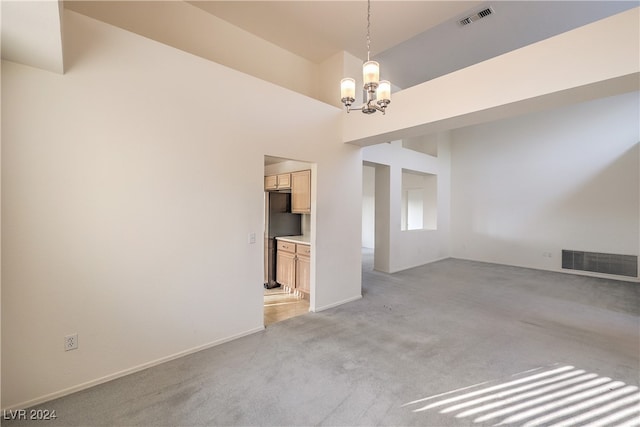 carpeted spare room with a high ceiling and a notable chandelier