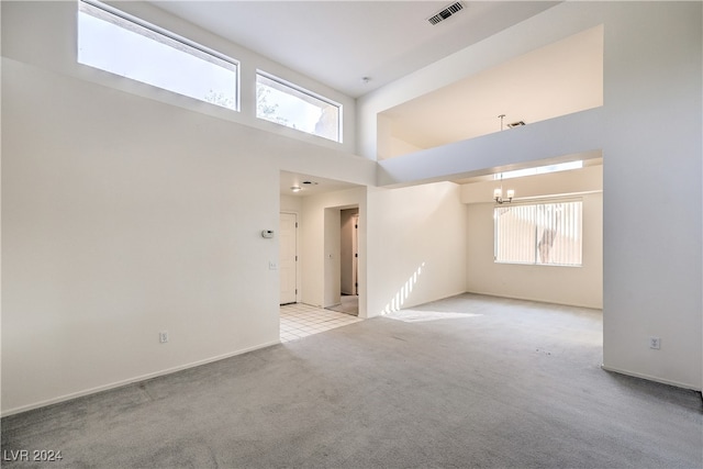 carpeted empty room featuring a chandelier, a high ceiling, and a wealth of natural light