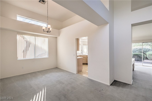 carpeted empty room featuring an inviting chandelier and a high ceiling