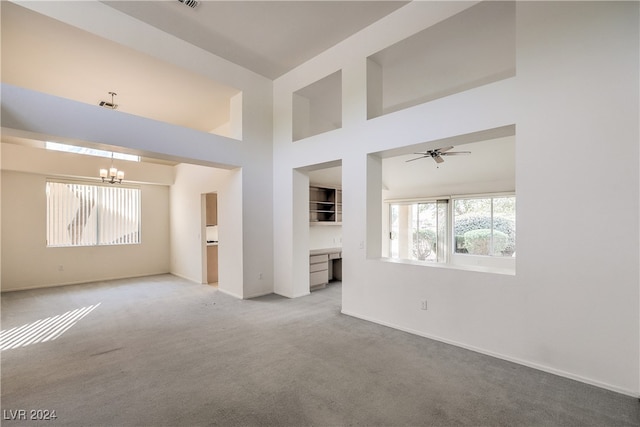 unfurnished living room with ceiling fan with notable chandelier, a towering ceiling, and light colored carpet