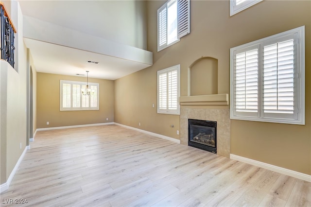 unfurnished living room featuring light hardwood / wood-style flooring, a tile fireplace, a chandelier, and a wealth of natural light