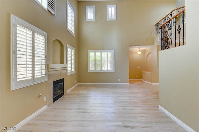 unfurnished living room with a high ceiling, a fireplace, light hardwood / wood-style floors, and a healthy amount of sunlight