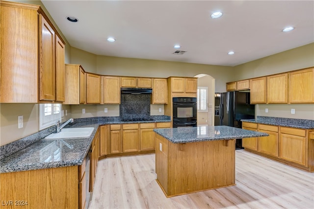 kitchen with sink, a kitchen island, light hardwood / wood-style flooring, black appliances, and dark stone countertops