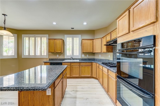 kitchen featuring dark stone counters, light hardwood / wood-style floors, hanging light fixtures, a kitchen island, and black appliances