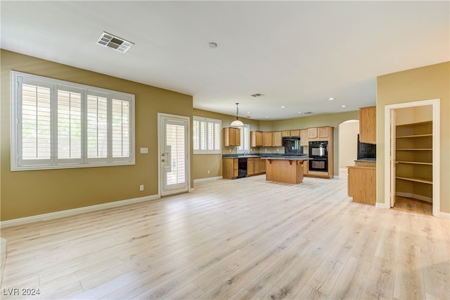 kitchen with hanging light fixtures, tasteful backsplash, a kitchen island, black appliances, and light hardwood / wood-style flooring