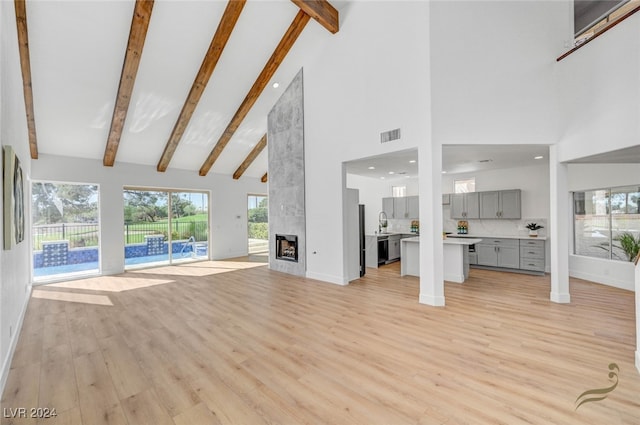 unfurnished living room with light hardwood / wood-style floors, sink, high vaulted ceiling, beamed ceiling, and a fireplace