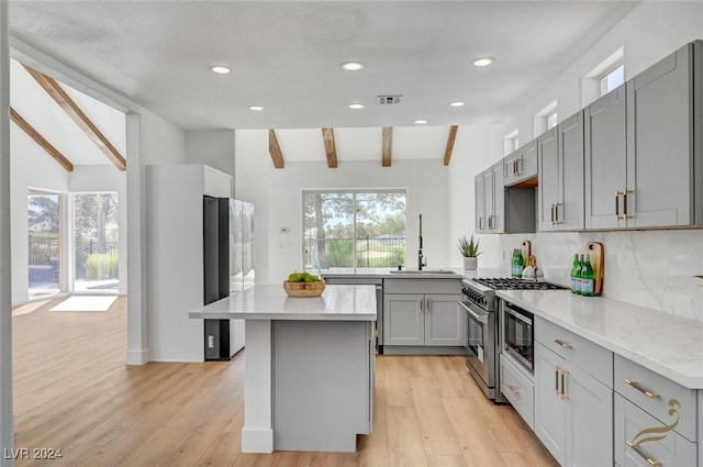 kitchen with light wood-type flooring, gray cabinetry, vaulted ceiling with beams, and appliances with stainless steel finishes