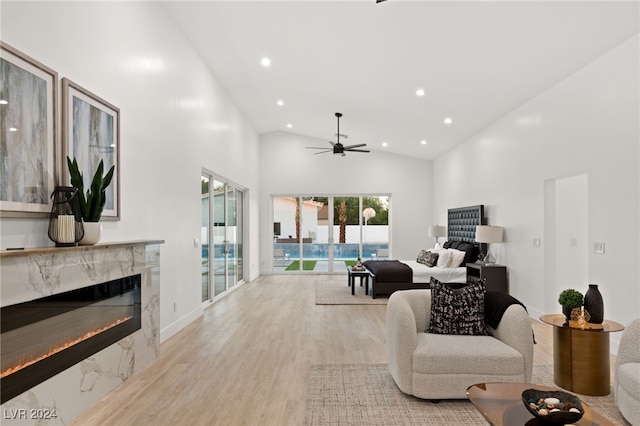 living room with high vaulted ceiling, light wood-type flooring, a premium fireplace, and ceiling fan