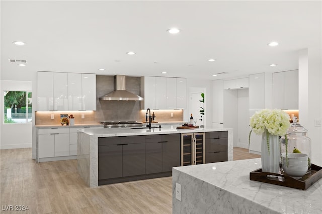 kitchen featuring light hardwood / wood-style flooring, white cabinetry, wall chimney range hood, and wine cooler