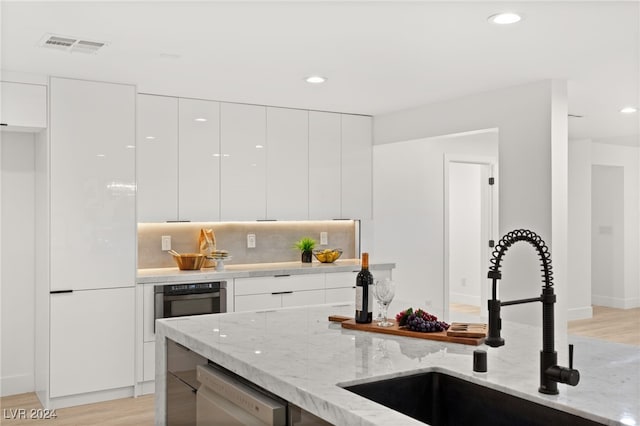 kitchen featuring light stone counters, dishwasher, sink, white cabinets, and stainless steel oven