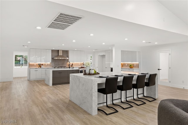 kitchen featuring a large island, wall chimney range hood, white cabinetry, a breakfast bar, and light wood-type flooring