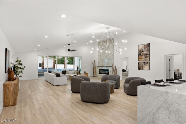 living room featuring ceiling fan with notable chandelier, light hardwood / wood-style floors, a high end fireplace, and high vaulted ceiling