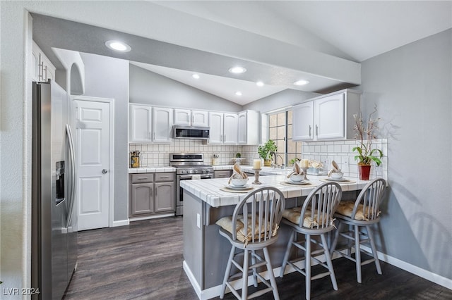 kitchen featuring a kitchen breakfast bar, white cabinets, kitchen peninsula, stainless steel appliances, and dark hardwood / wood-style floors