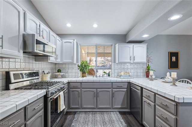 kitchen featuring gray cabinetry, stainless steel appliances, kitchen peninsula, and dark hardwood / wood-style flooring