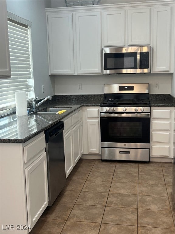 kitchen with dark tile patterned flooring, appliances with stainless steel finishes, sink, white cabinetry, and dark stone countertops