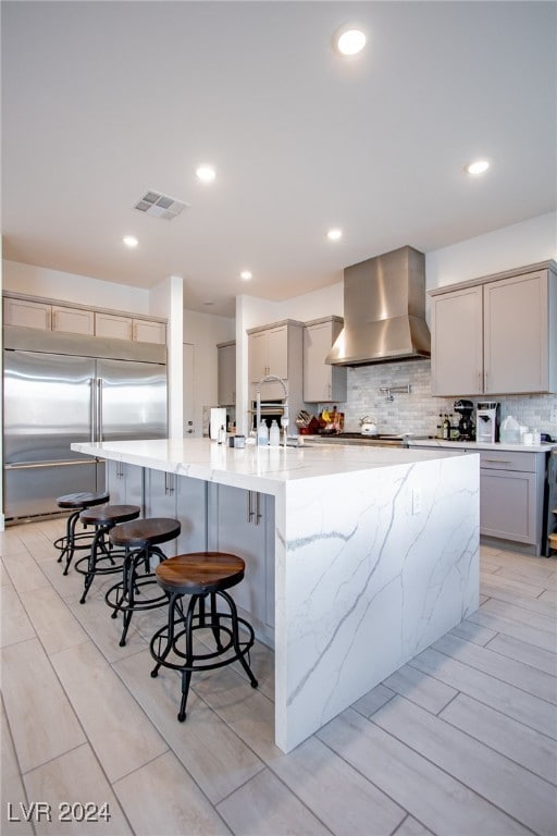 kitchen featuring wall chimney exhaust hood, built in refrigerator, gray cabinets, and a spacious island