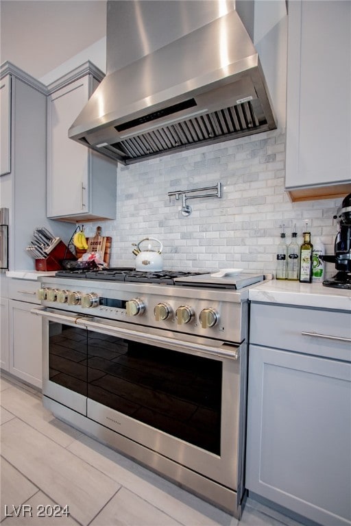 kitchen featuring light tile patterned flooring, backsplash, wall chimney exhaust hood, gray cabinets, and range with two ovens