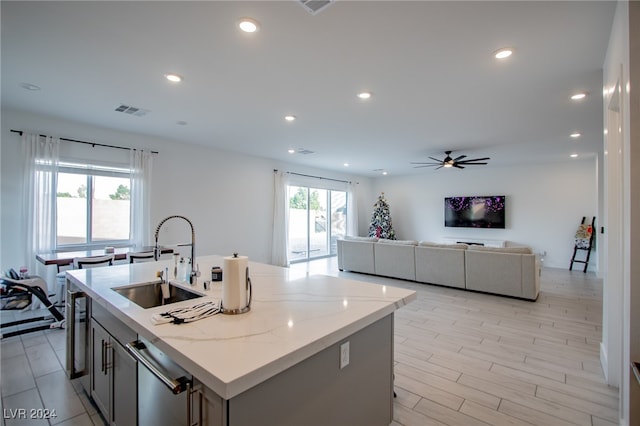 kitchen with light stone counters, ceiling fan, sink, stainless steel dishwasher, and a center island with sink