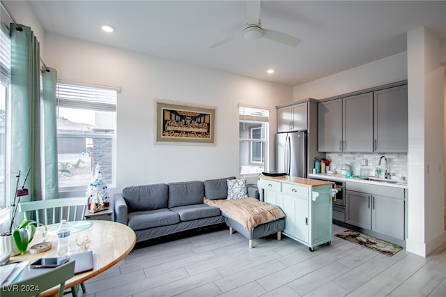 living room featuring light wood-type flooring, a healthy amount of sunlight, sink, and ceiling fan