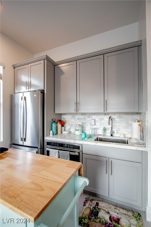 kitchen with stainless steel appliances, sink, wooden counters, and decorative backsplash