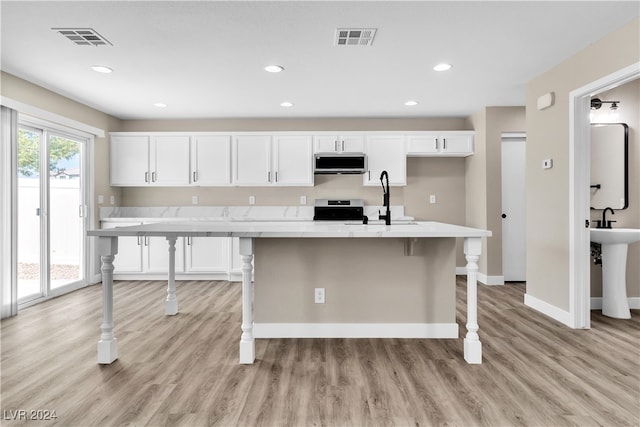 kitchen featuring white cabinetry, a kitchen bar, light hardwood / wood-style flooring, a center island with sink, and appliances with stainless steel finishes