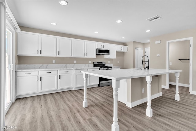 kitchen with an island with sink, stainless steel appliances, white cabinetry, and light hardwood / wood-style floors