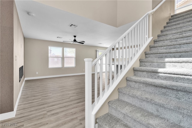 staircase featuring ceiling fan, hardwood / wood-style flooring, and a fireplace