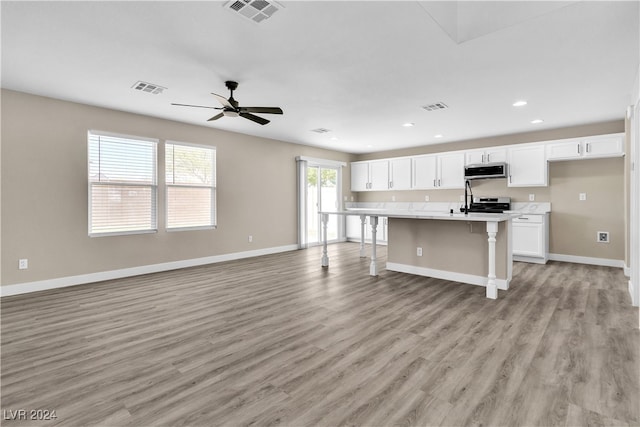 kitchen with white cabinetry, light hardwood / wood-style flooring, a kitchen breakfast bar, a center island with sink, and ceiling fan