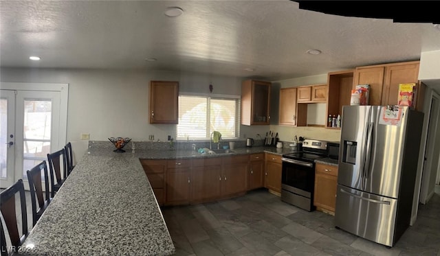 kitchen featuring light stone counters, sink, kitchen peninsula, french doors, and appliances with stainless steel finishes