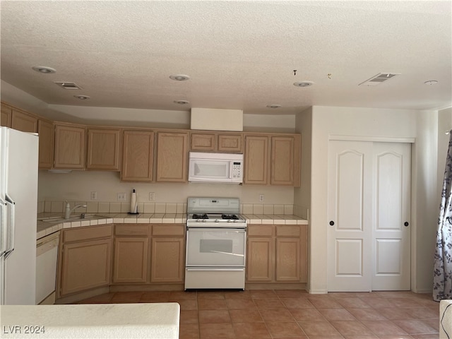 kitchen featuring sink, a textured ceiling, tile counters, and white appliances