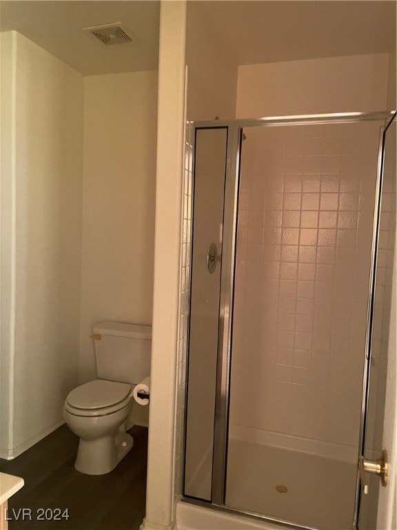 bathroom with hardwood / wood-style floors, toilet, and an enclosed shower