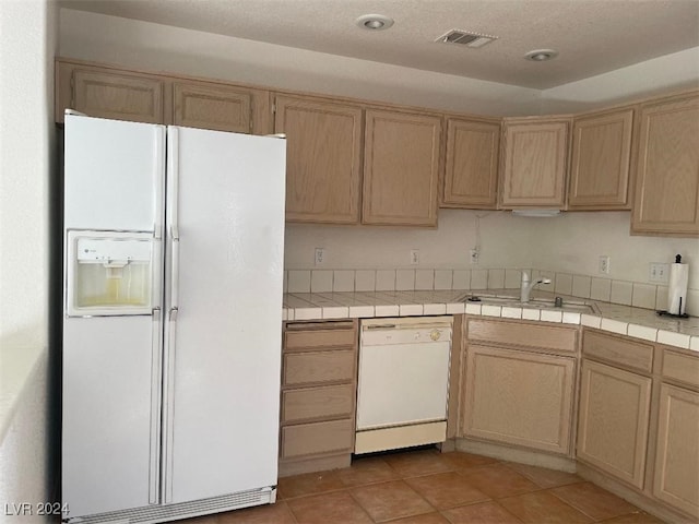 kitchen with white appliances, light brown cabinets, light tile patterned floors, tile counters, and sink