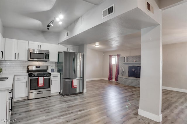 kitchen featuring tasteful backsplash, white cabinetry, a brick fireplace, light wood-type flooring, and stainless steel appliances