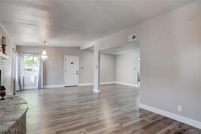 unfurnished living room featuring hardwood / wood-style flooring, a textured ceiling, lofted ceiling, and a stone fireplace