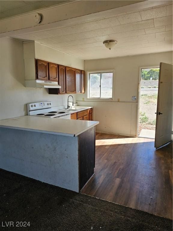 kitchen with light countertops, dark wood-type flooring, under cabinet range hood, electric stove, and a sink