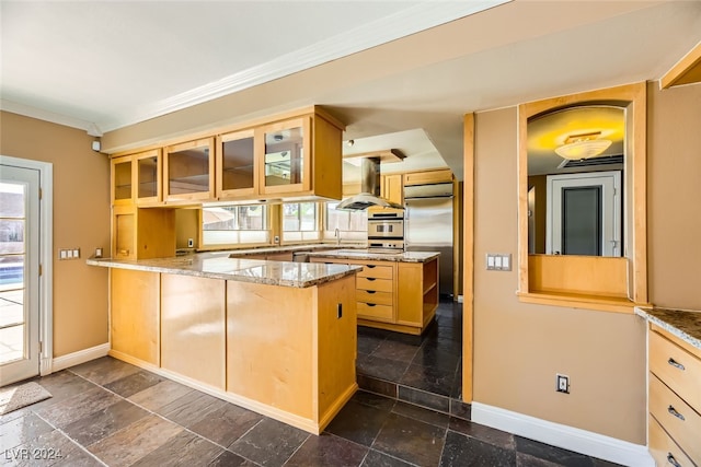 kitchen with light stone counters, kitchen peninsula, island range hood, built in refrigerator, and light brown cabinetry