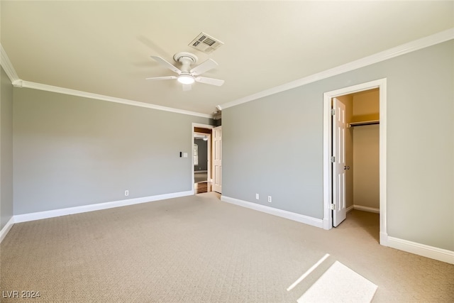 unfurnished bedroom with ornamental molding, light carpet, ceiling fan, and a walk in closet