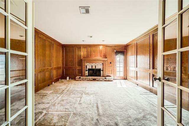 unfurnished living room featuring a fireplace, wood walls, light carpet, and french doors