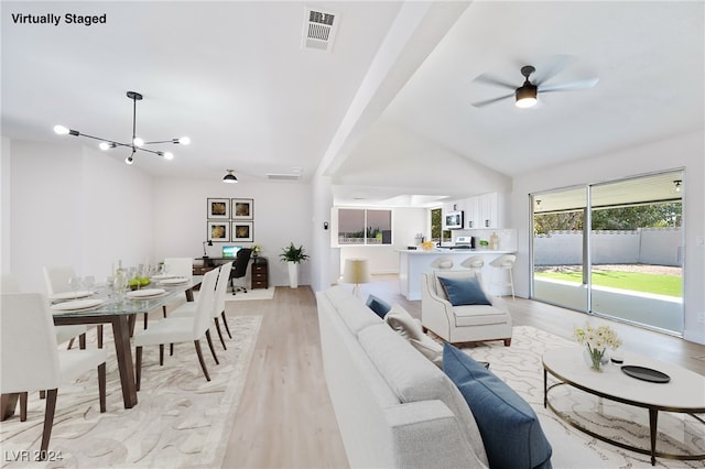 living room with vaulted ceiling, ceiling fan with notable chandelier, and light wood-type flooring