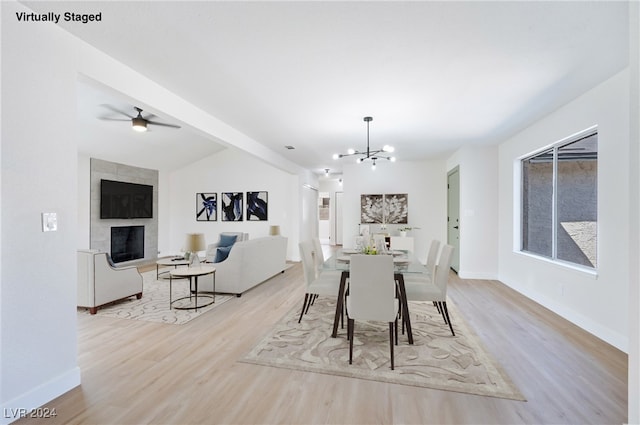 dining room featuring a fireplace, lofted ceiling, light wood-type flooring, and ceiling fan with notable chandelier