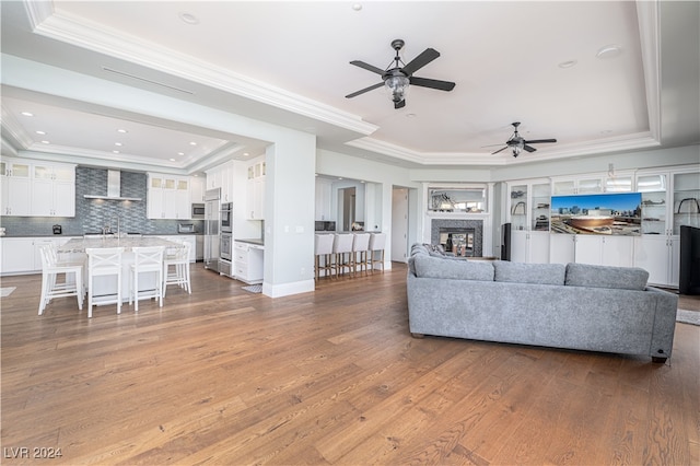 living room featuring hardwood / wood-style floors, ceiling fan, a raised ceiling, and ornamental molding