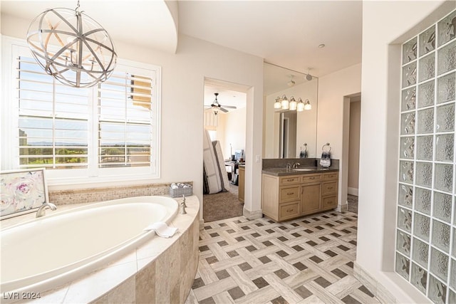 bathroom with tiled bath, vanity, and ceiling fan with notable chandelier