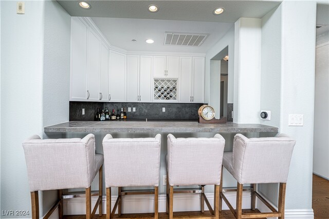 bar with decorative backsplash, white cabinetry, and dark hardwood / wood-style flooring