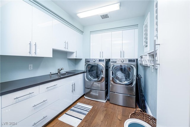 washroom featuring washing machine and clothes dryer, dark hardwood / wood-style flooring, sink, and cabinets