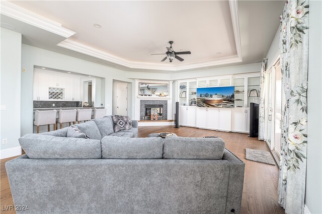 living room featuring ceiling fan, wood-type flooring, crown molding, and a tray ceiling