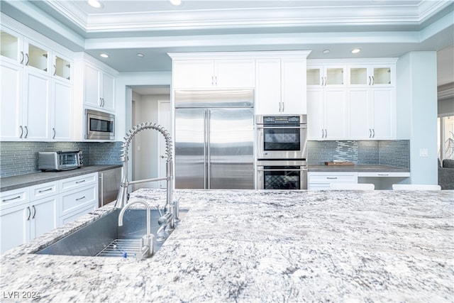 kitchen with built in appliances, white cabinets, and crown molding