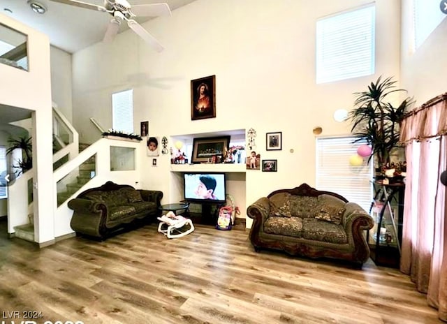 living room with ceiling fan, a towering ceiling, and hardwood / wood-style floors